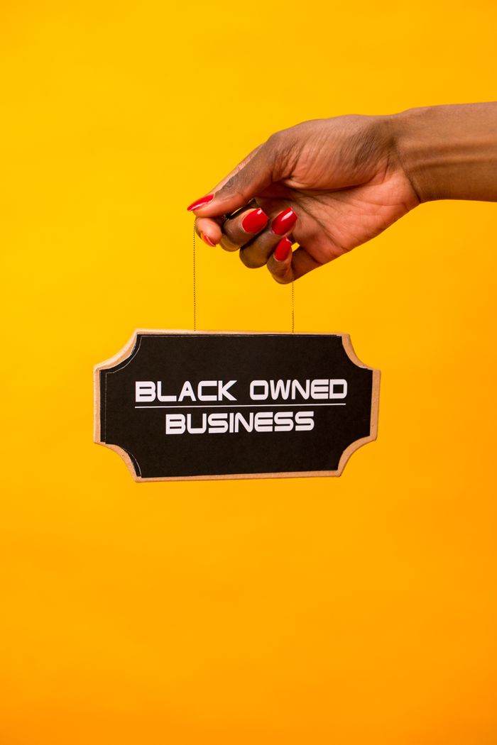 A hand holds a Black Owned Business sign against a vibrant yellow background.