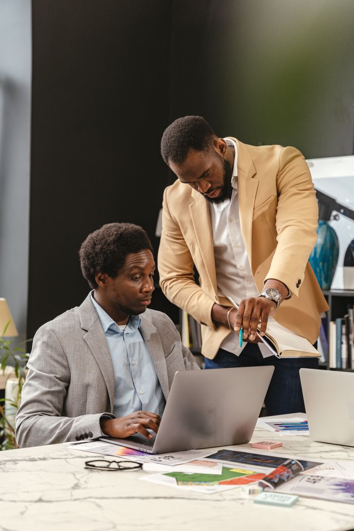 Two business professionals working together in an office space with laptops and papers.